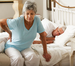 Woman sitting on bed suffering from lower back pain